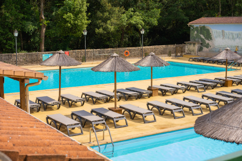 Piscina all'aperto con lettini e ombrelloni al Camping La Clémentine, villaggio vacanze in Occitania, Francia.