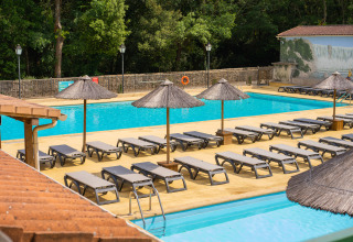 Piscina all'aperto con lettini e ombrelloni al Camping La Clémentine, villaggio vacanze in Occitania, Francia.