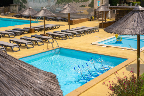 Außenpoolbereich im Camping La Clémentine mit Liegen, Strohdächern und Aquabikes im Pool.