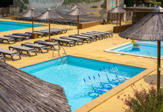 Espace piscine extérieur au Camping La Clémentine avec transats, parasols et vélos aquatiques dans l’eau.