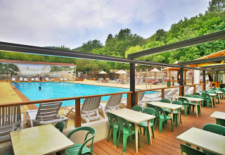 Udendørs swimmingpool og terrasse med borde og grønne stole på Camping La Clémentine i Occitanie, Frankrig.