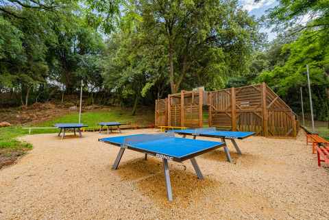 Mesas de ping-pong al aire libre y zona de juegos rodeadas de árboles en Camping La Clémentine, Occitania, Francia.