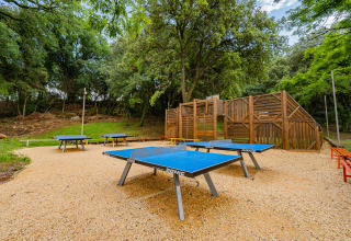 Tavoli da ping pong all'aperto e area giochi circondata da alberi al Camping La Clémentine in Occitania, Francia.
