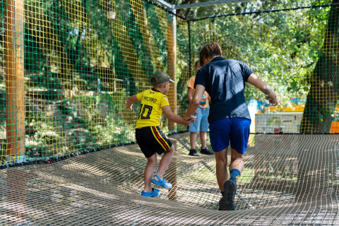 Bambini che giocano su una rete sospesa in un parco avventura al Camping La Clémentine, Occitania, Francia.