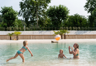 Een gezin speelt met een strandbal in het ondiepe zwembad van Camping La Clémentine in Occitanië, Frankrijk.