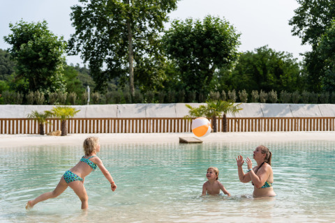 Une famille joue avec un ballon de plage dans la piscine peu profonde du Camping La Clémentine, Occitanie, France.
