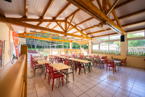 Comedor con sillas de colores y vista al jardín en Camping La Clémentine, parque vacacional en Occitania, Francia.