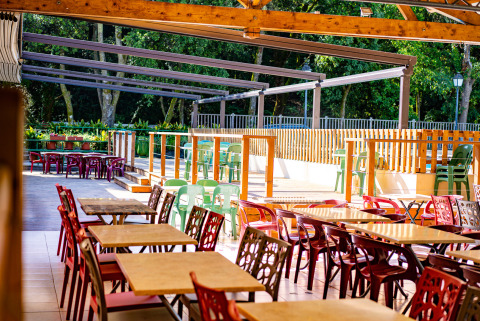 Zona de comedor al aire libre con sillas y mesas de colores en Camping La Clémentine en Occitania, Francia.