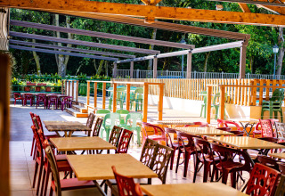 Udendørs spiseområde med tomme borde og farverige stole på Camping La Clémentine i Occitanie, Frankrig.