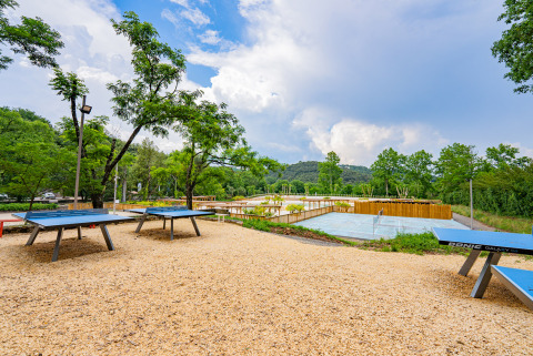 Mesas de ping-pong al aire libre y pista de tenis rodeadas de naturaleza en Camping La Clémentine, Occitania, Francia.