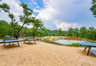Udendørs bordtennisborde og tennisbane omgivet af grøn natur på Camping La Clémentine i Occitanie, Frankrig.