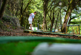 Un uomo gioca a mini golf in un campeggio immerso nel verde a Camping La Clémentine in Occitania, Francia.