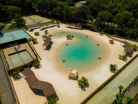 Veduta aerea di una spiaggia artificiale e laguna al Camping La Clémentine, immersa nel verde in Occitania, Francia.
