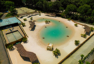 Veduta aerea di una spiaggia artificiale e laguna al Camping La Clémentine, immersa nel verde in Occitania, Francia.
