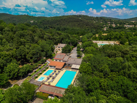 Aerial view of Camping La Clémentine holiday park in Occitanie, France, featuring pools amid lush forest.