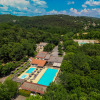 Aerial view of Camping La Clémentine holiday park in Occitanie, France, featuring pools amid lush forest.