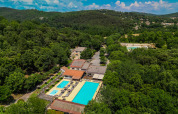 Vista aérea de Camping La Clémentine en Occitania, Francia, mostrando piscinas entre bosque frondoso.