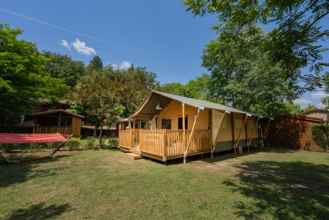 Tienda glamping y hamaca en Camping La Clémentine, un parque vacacional en Occitania, Francia, entre árboles.