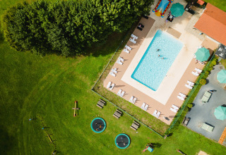 Luftfoto af swimmingpool, liggestole og legeområde med trampoliner i ferieparken Camping La Colline, Belgien.