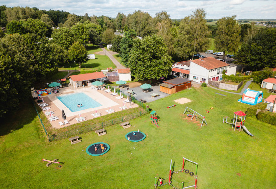Vista aerea di Camping La Colline in Belgio con piscina, area giochi e tanto verde nel villaggio vacanze.