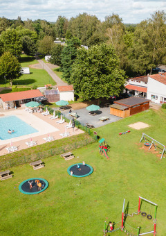 Vista aérea de Camping La Colline en Bélgica con piscina, parque infantil y zonas verdes en el parque vacacional.