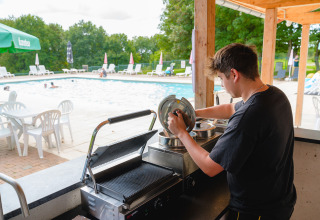 Persoon bereidt voedsel aan poolbar in Camping La Colline vakantiedomein in Belgisch Luxemburg.