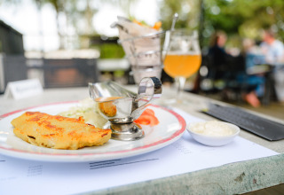 Close-up of a delicious meal served outdoors at Camping La Colline, Belgium Luxembourg, with a drink behind.
