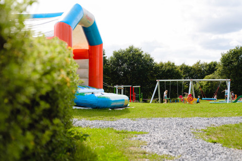 Parque infantil con castillo hinchable, columpios y niños jugando en Camping La Colline, Bélgica.