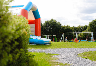 Speeltuin met springkussen, schommels en spelende kinderen op Camping La Colline in België.