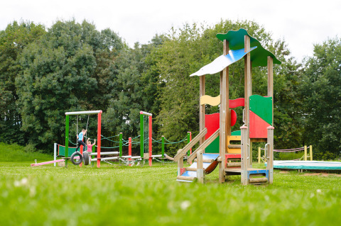 Colorful playground with children and green trees at Camping La Colline, Belgium Luxembourg holiday park.