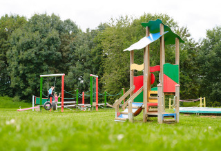 Colorful playground with children and green trees at Camping La Colline, Belgium Luxembourg holiday park.