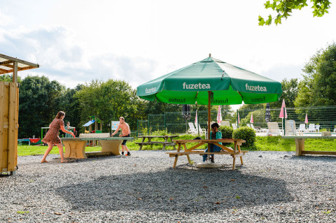 Outdoor area of Camping La Colline, Belgium, with table tennis and green FuzeTea umbrellas in summer.