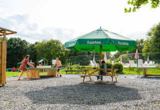 Zomerterras in Camping La Colline, België, met tafeltennis en groene FuzeTea-parasol in de buitenlucht.