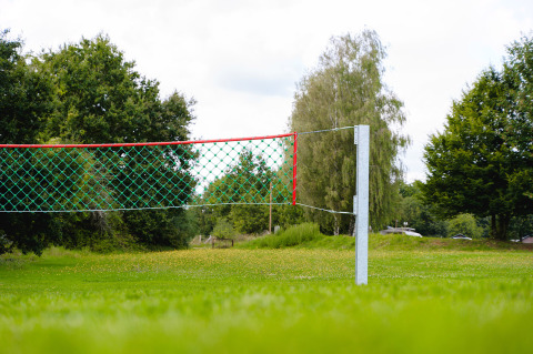 Camping La Colline: Volleyball net on grassy field surrounded by trees at holiday park in Belgium Luxembourg.