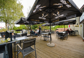 Espace de restauration extérieur avec parasols et terrasse en bois au Camping La Colline, Belgique Luxembourg.