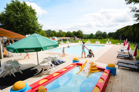 Outdoor pool area at Camping La Colline, Belgium, with sun loungers, kids' pool, and families enjoying the sun.