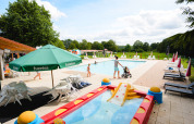 Udendørs poolområde på Camping La Colline, Belgien, med liggestole, børnepool og familier ved vandet.