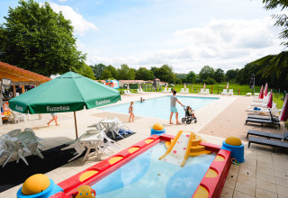 Outdoor pool area at Camping La Colline, Belgium, with sun loungers, kids' pool, and families enjoying the sun.