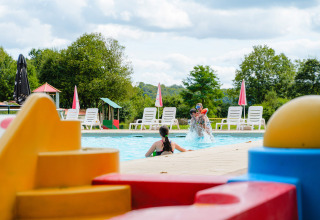 Børn leger i en swimmingpool med farverige legetøjsklodser i forgrunden på Camping La Colline, Belgien.