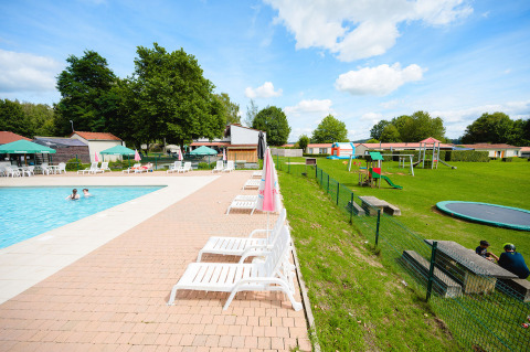 Outdoor pool area with sun loungers, playground, and greenery at Camping La Colline holiday park in Belgium.