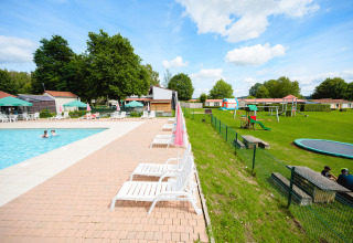 Outdoor pool area with sun loungers, playground, and greenery at Camping La Colline holiday park in Belgium.