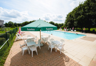 Outdoor swimming pool at Camping La Colline, Belgium, with sun loungers, tables and green Fuzetea umbrellas.