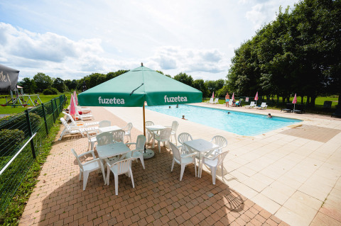 Outdoor swimming pool at Camping La Colline, Belgium, with sun loungers, tables and green Fuzetea umbrellas.