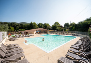 Udendørs swimmingpool med solsenge og gæster, omgivet af grønne bakker på Camping La Garenne i Frankrig.