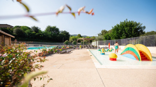 Family-friendly pool area with colorful play equipment and loungers at Camping La Garenne, France.