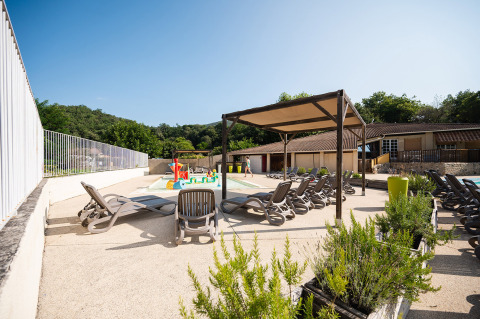 Area piscina all'aperto con lettini, tenda da sole e spazio giochi al Camping La Garenne, Francia.