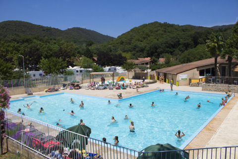 Personas disfrutando de la piscina al aire libre en el Camping La Garenne, Auvergne-Rhône-Alpes, Francia, rodeados de colinas.