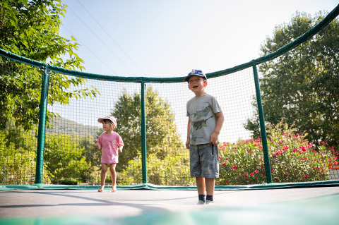 Two children play on a trampoline at Camping La Garenne in Auvergne-Rhône-Alpes, surrounded by greenery.