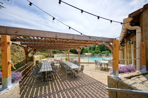 Terrazza esterna con tavoli e sedie sotto una pergola a Camping La Garenne, Auvergne-Rhône-Alpes, Francia.