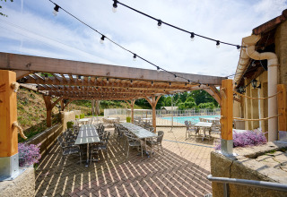 Terrazza esterna con tavoli e sedie sotto una pergola a Camping La Garenne, Auvergne-Rhône-Alpes, Francia.
